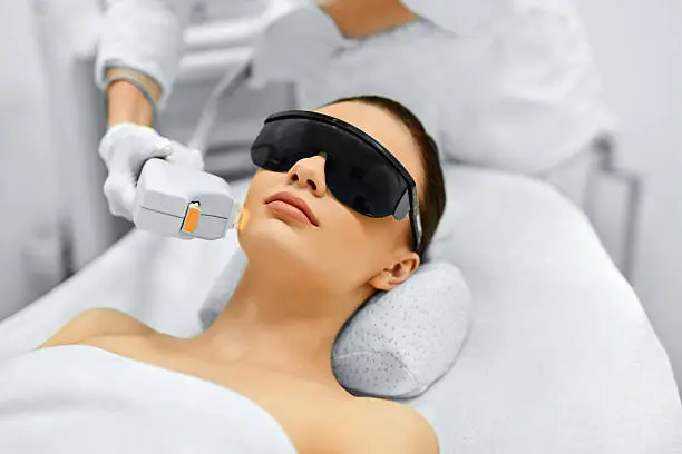 Skincare professional evaluating facial texture under bright task lighting with precision tools