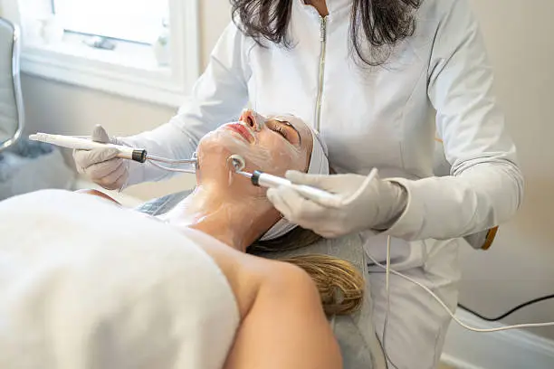 Aesthetic provider assessing skin condition carefully with magnifying lamp and treatment notes
